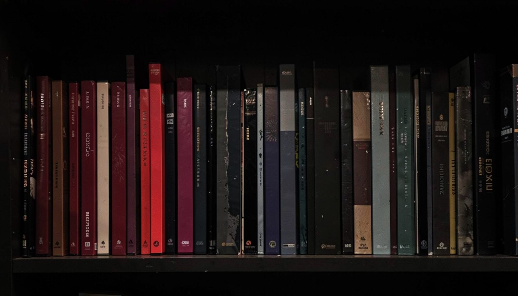 A dark, moody shelf display with DVD cases in deep reds, blacks, and muted grays, softly lit from above against a shadowed background